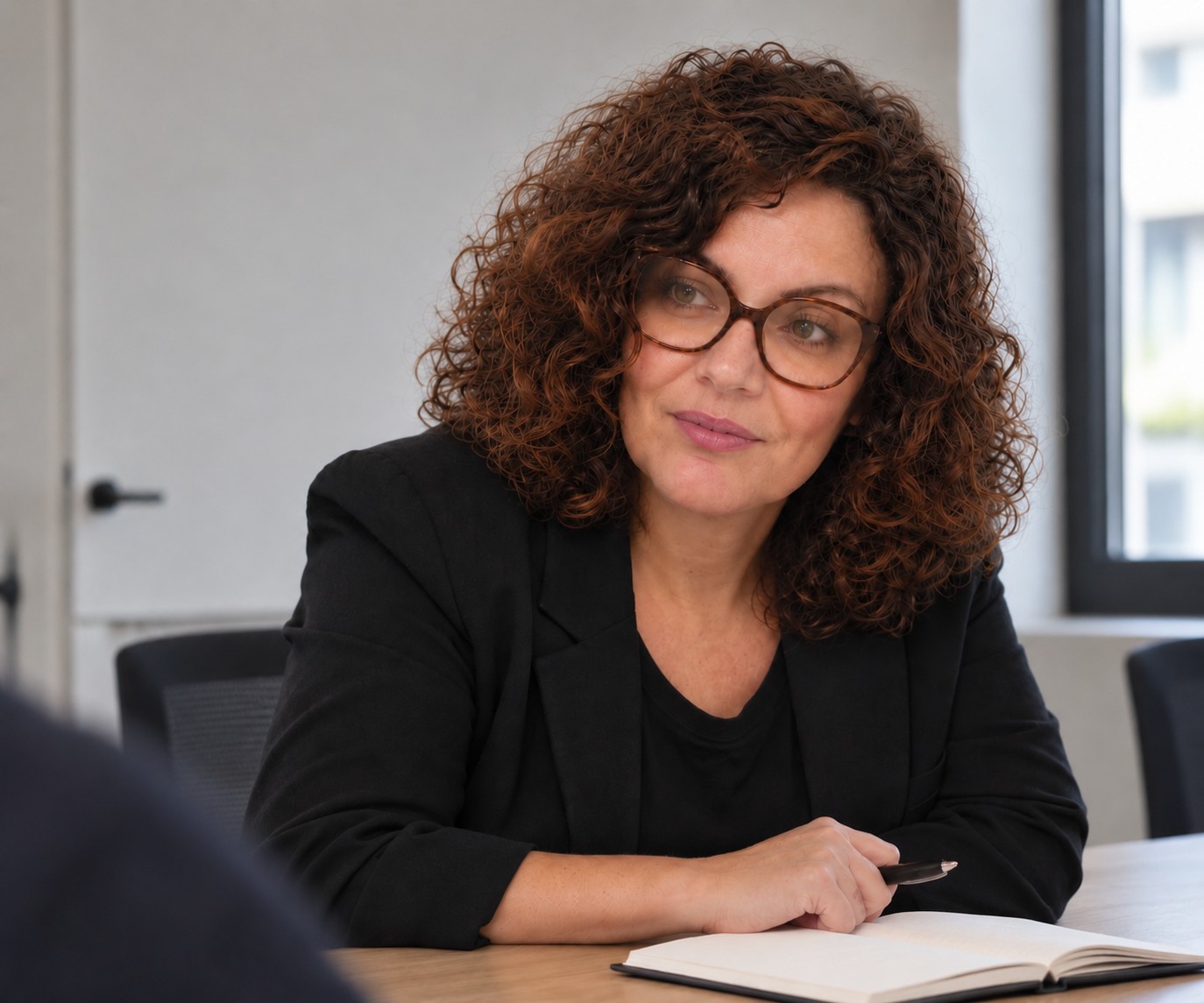 Myriam Prette-Girerd en réunion de travail, carnet ouvert et stylo en main, échangeant avec une personne au premier plan.